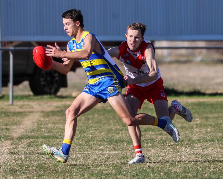 MCUE forward Flynn Collins attempts to get a kick away while being tackled by Griffith's James Girdler during the clash between the Goannas and Swans at Mangoplah Sportsground. Picture by Les Smith